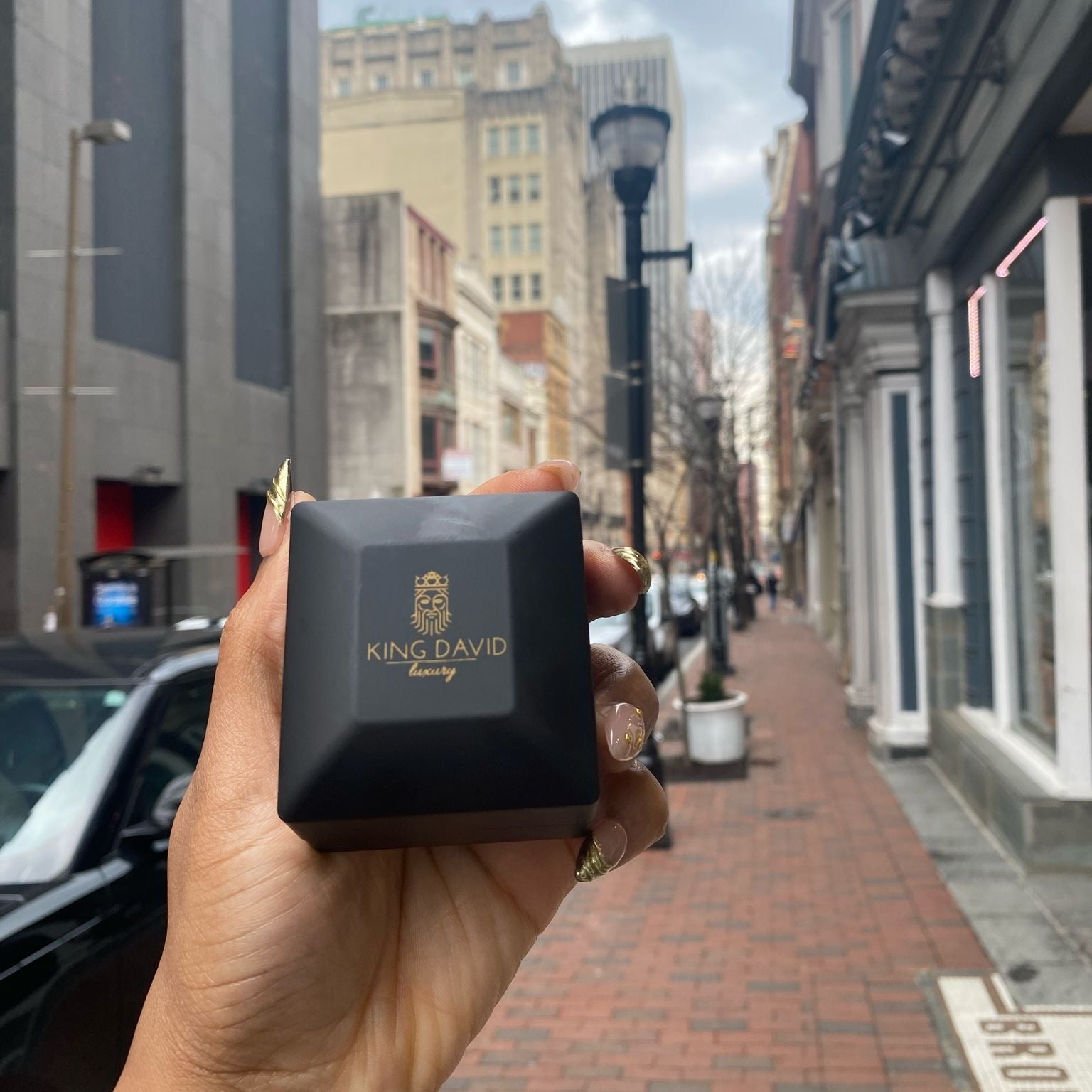 Hand holding a black jewelry box on a city street.