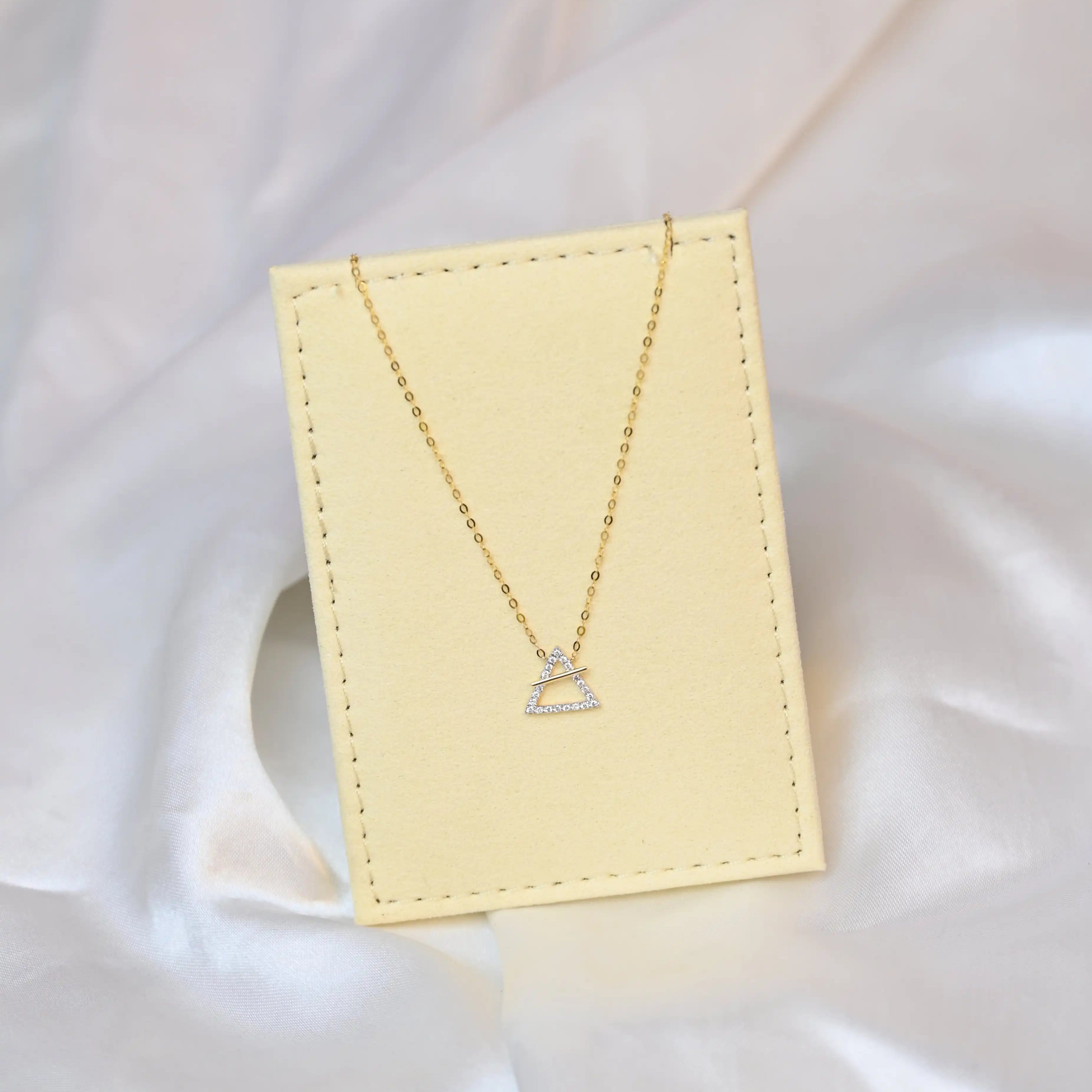 18K yellow gold necklace with crossed triangle diamond pendant – minimalist geometric gold jewelry for women on a beige jewelry display