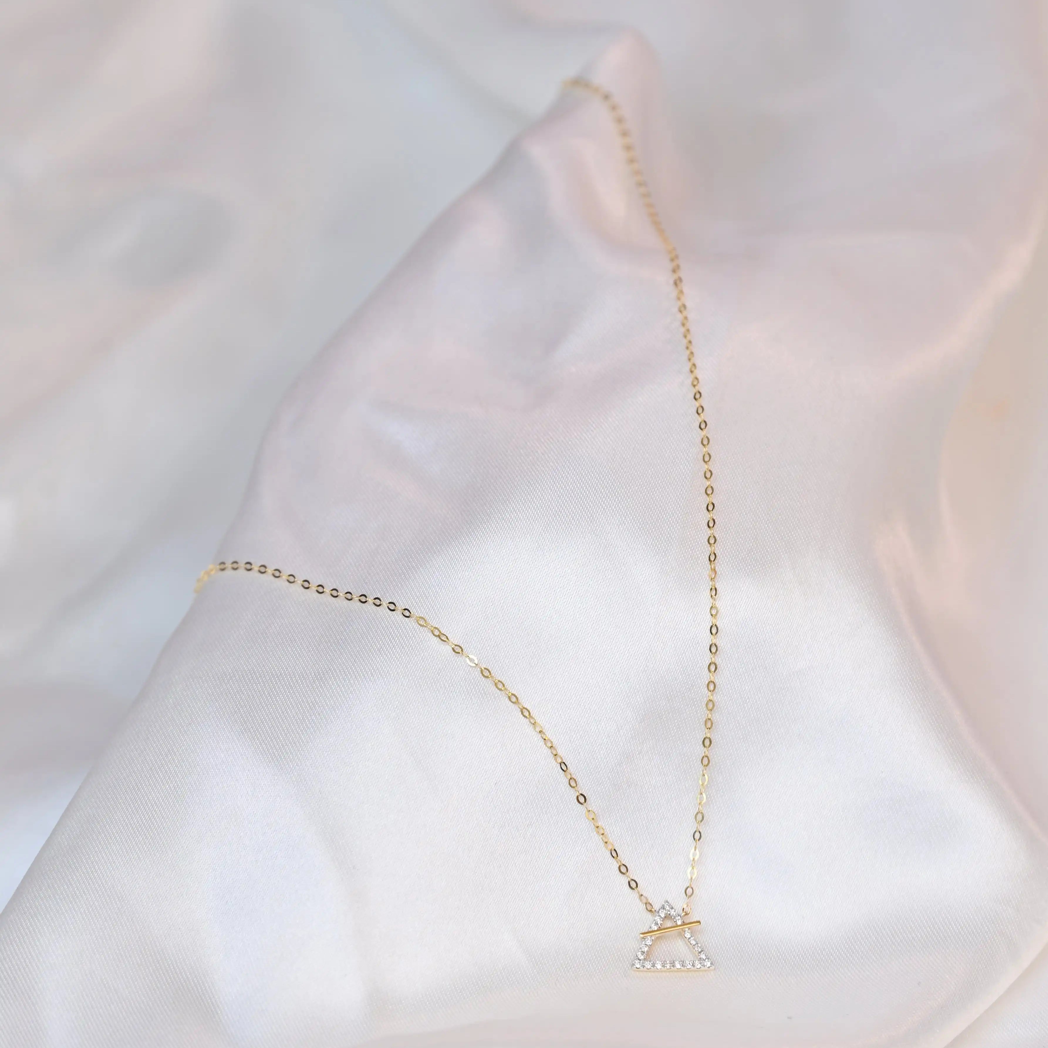 18K yellow gold necklace with crossed triangle diamond pendant – minimalist geometric gold jewelry for women on a white silk cloth background