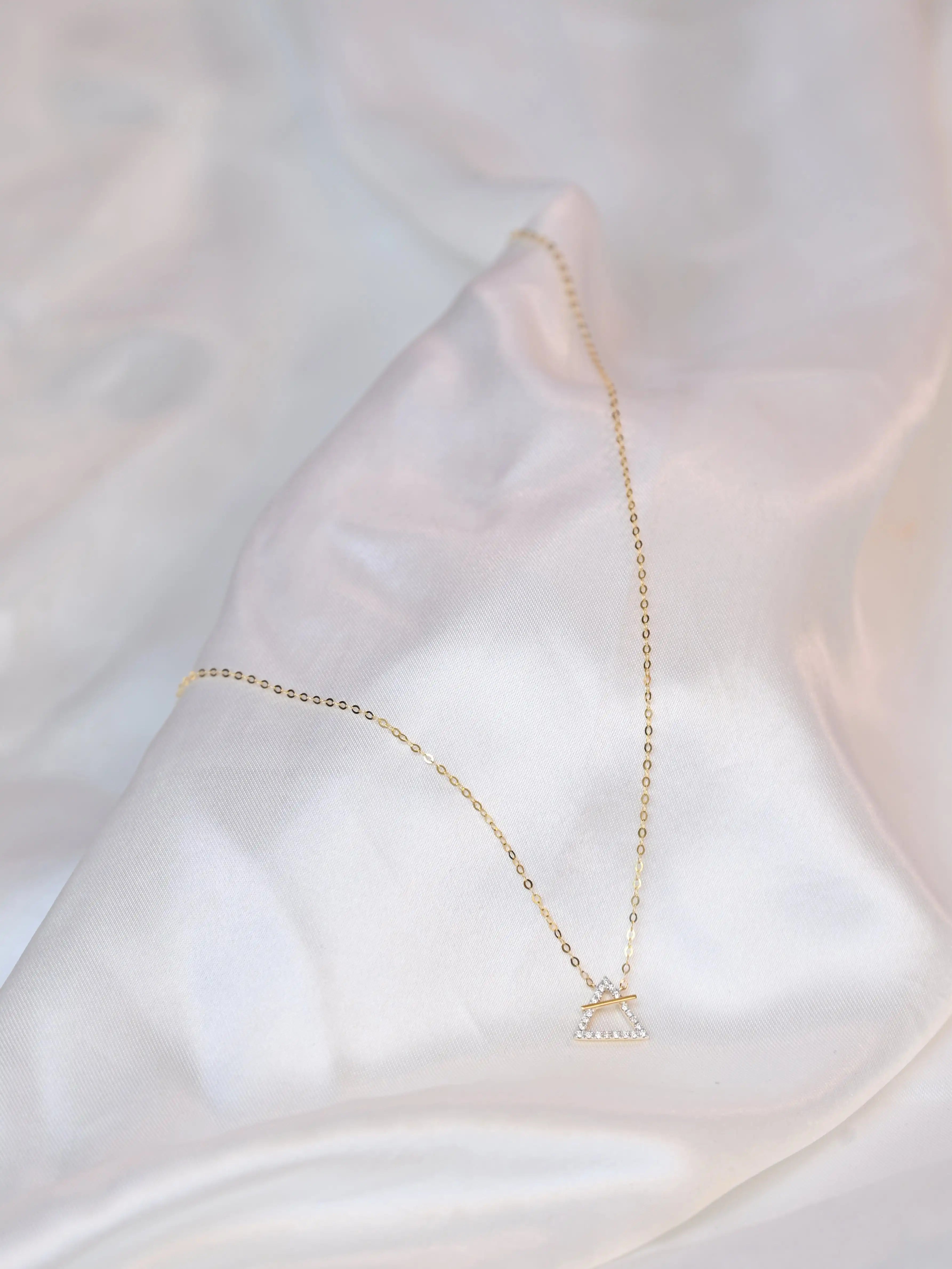 18K yellow gold necklace with crossed triangle diamond pendant – minimalist geometric gold jewelry for women on a white silk cloth background