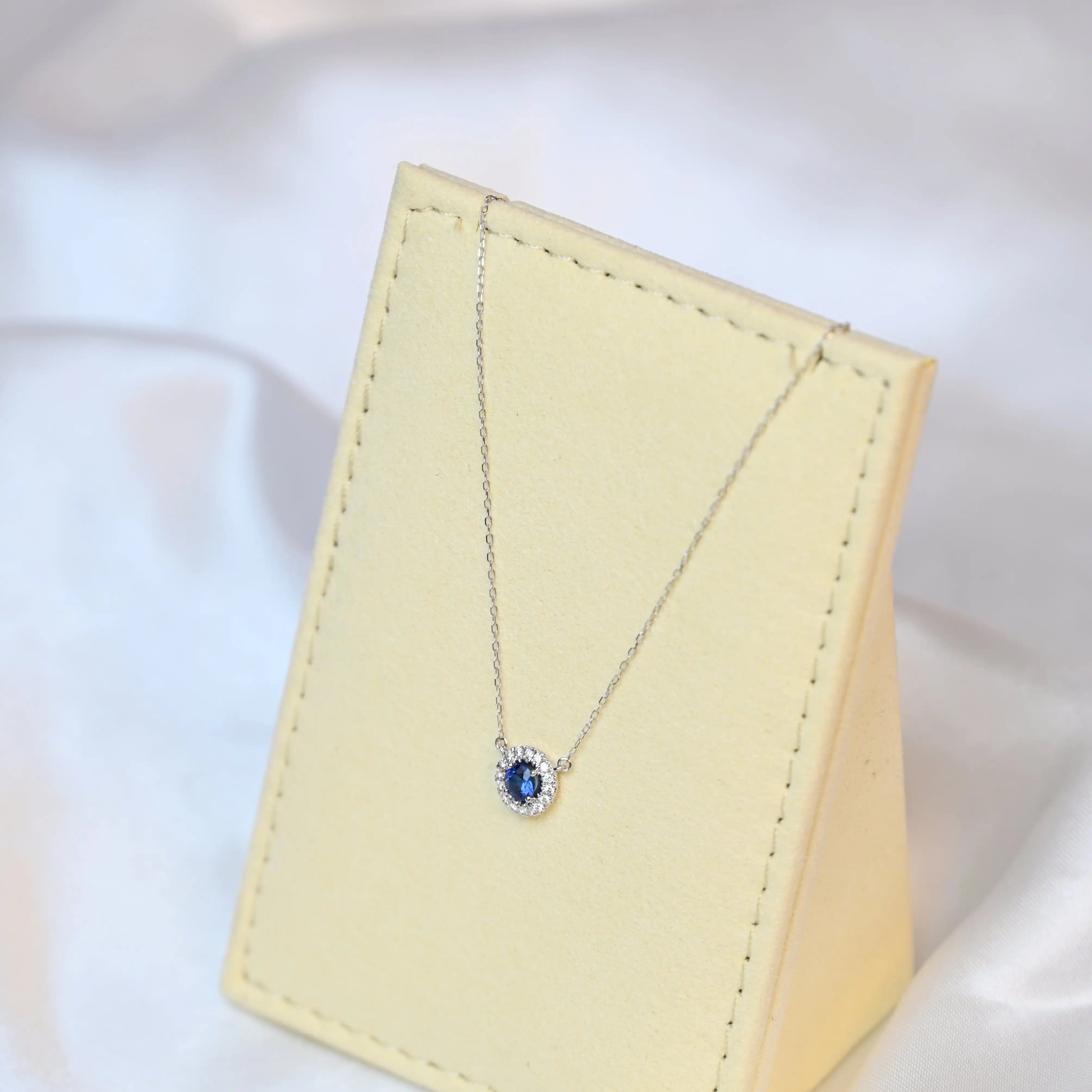 Michal Royalty Sapphire Necklace with royal blue center stone and round diamond halo in 18K white gold – luxury gemstone pendant for women on a beige jewelry display set