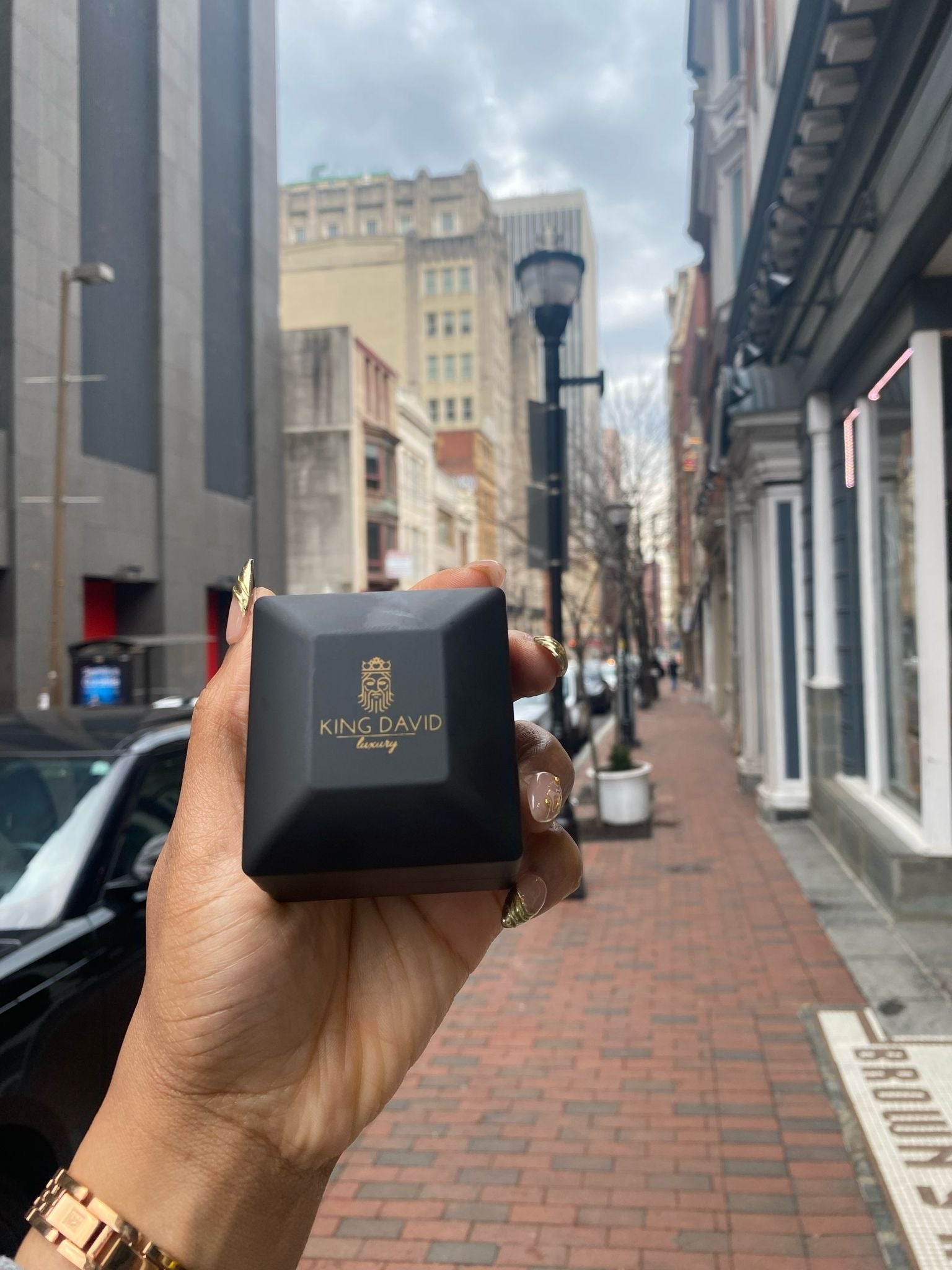 Hand holding a black jewelry box on a city street.