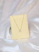 18K yellow gold necklace with crossed triangle diamond pendant – minimalist geometric gold jewelry for women on a beige jewelry display 