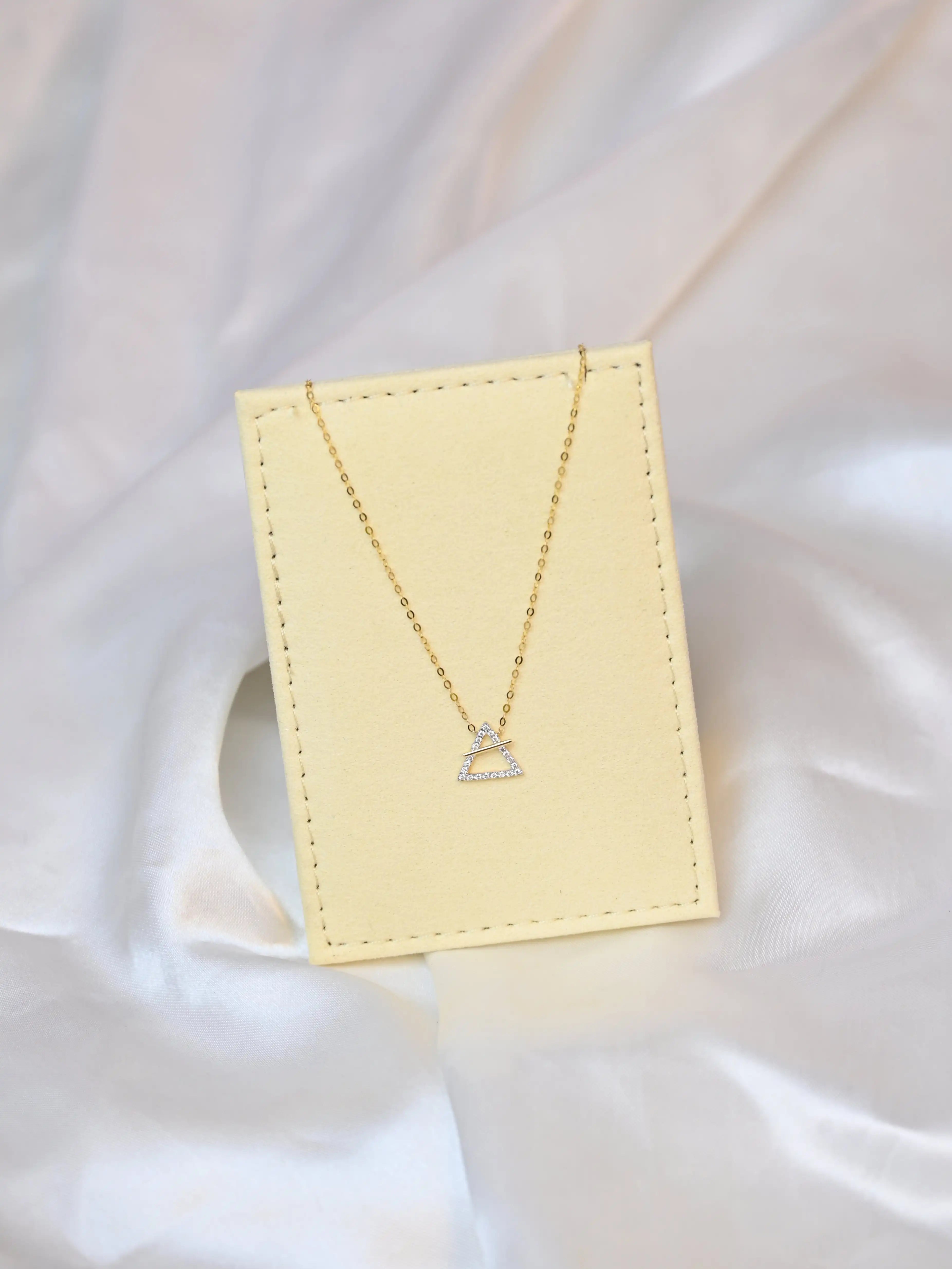 18K yellow gold necklace with crossed triangle diamond pendant – minimalist geometric gold jewelry for women on a beige jewelry display 
