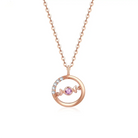 A delicate 18K rose gold necklace with a circular pendant featuring a round pink sapphire in the center and a curved row of small white diamonds on one side. The pendant hangs from a thin gold chain.