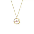 A delicate 18K yellow gold necklace with a circular pendant featuring a round pink sapphire in the center and a curved row of small white diamonds on one side. The pendant hangs from a thin gold chain.