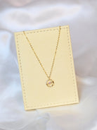 A delicate 18K yellow gold necklace with a circular pendant featuring a round pink sapphire in the center and a curved row of small white diamonds on one side. The pendant hangs from a thin gold chain.
